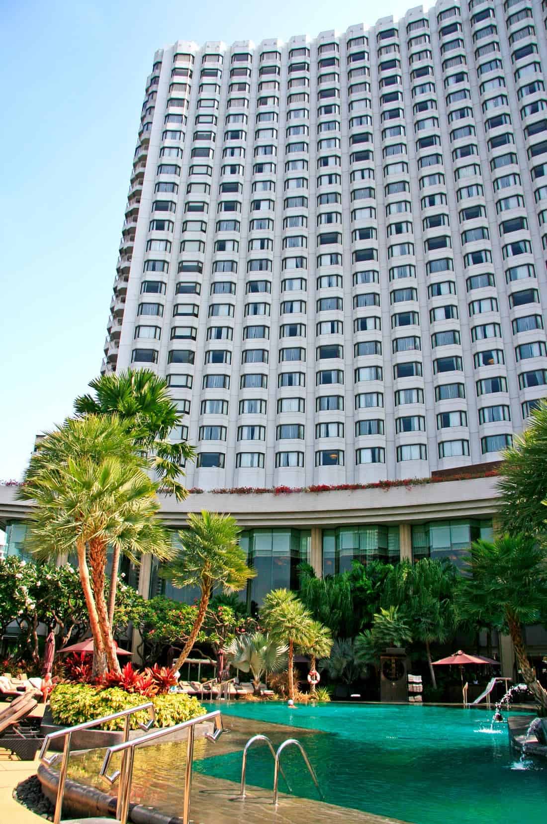 Tall white Shangri-La Wing rising above the hotelโs tropical gardens and turquoise swimming pool in Bangkok