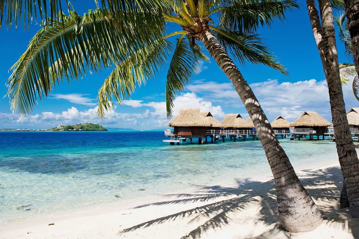 Wooden huts with thatch roofs on stilts in blue lagoon in Bora Bora