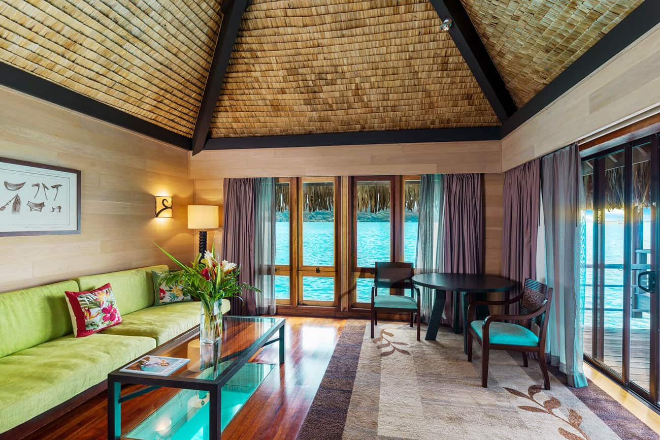 Living room in an overwater deluxe villa at St. Regis Bora Bora, with green couch and wood floors