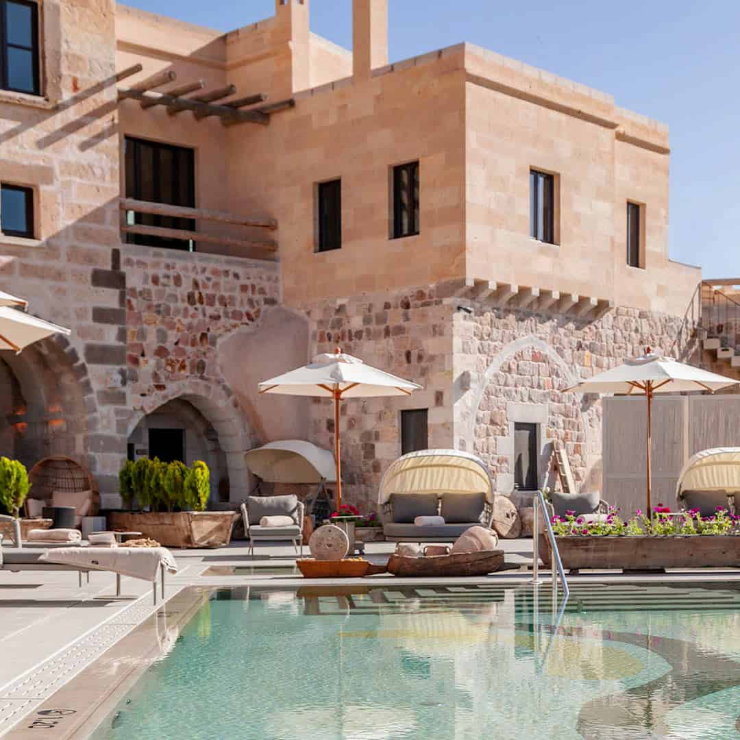 Hotel pool in front of stone building with pool loungers