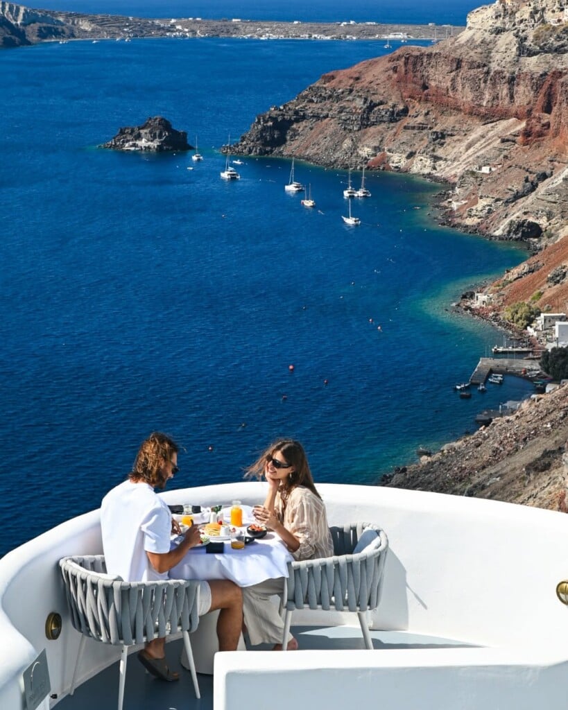 A couple eat breakfast with a view of the red cliffs of Oia, Santorini