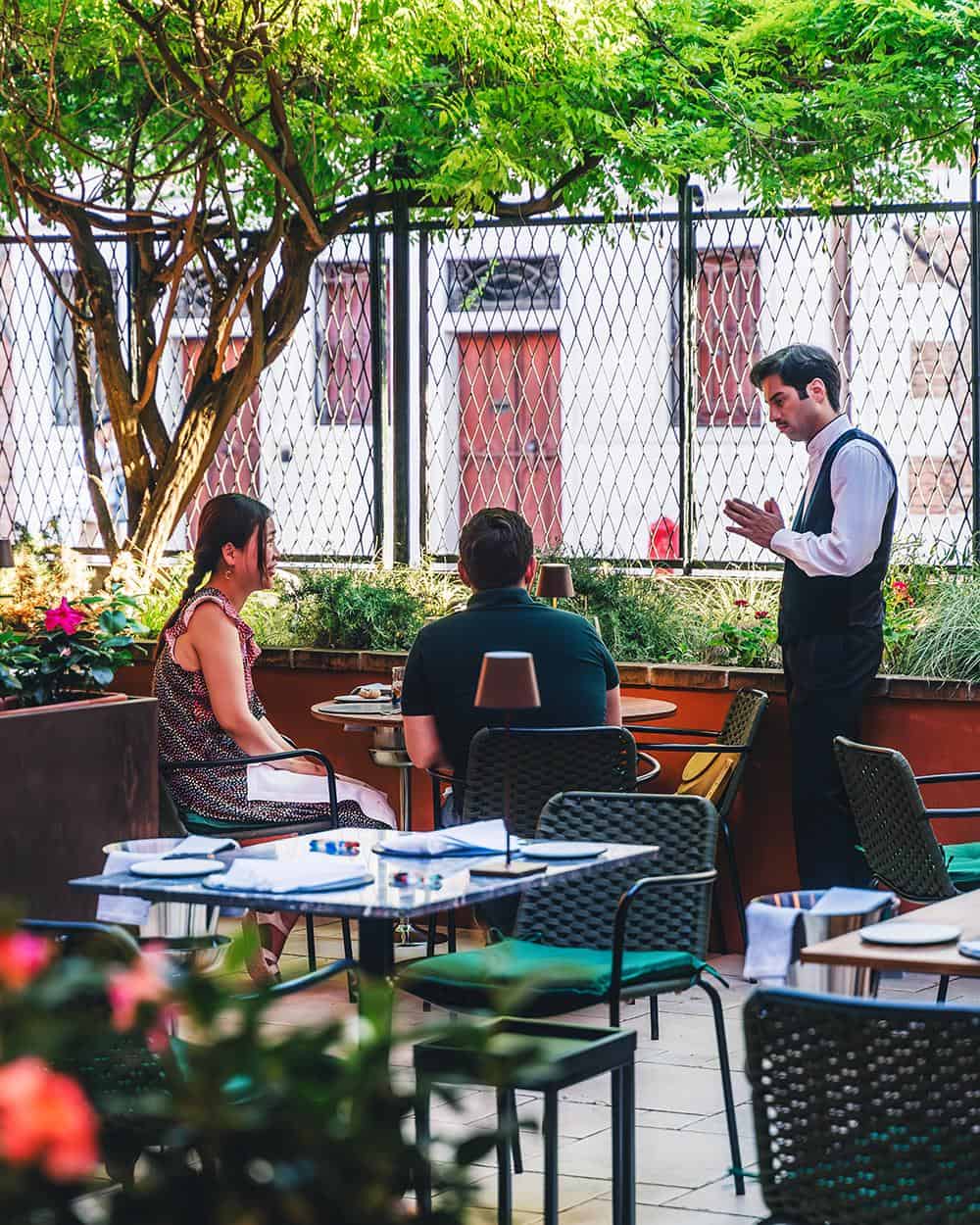 Waiter helping a couple in the Wisteria Restaurant courtyard