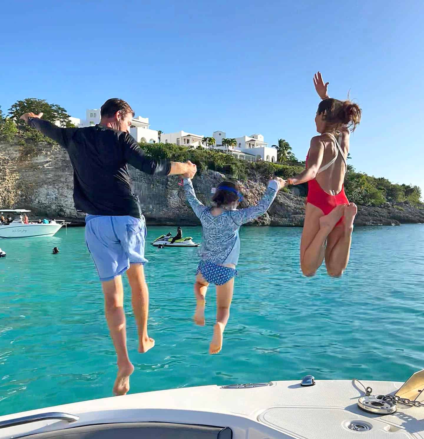Family of three jump off a boat into the turquoise water