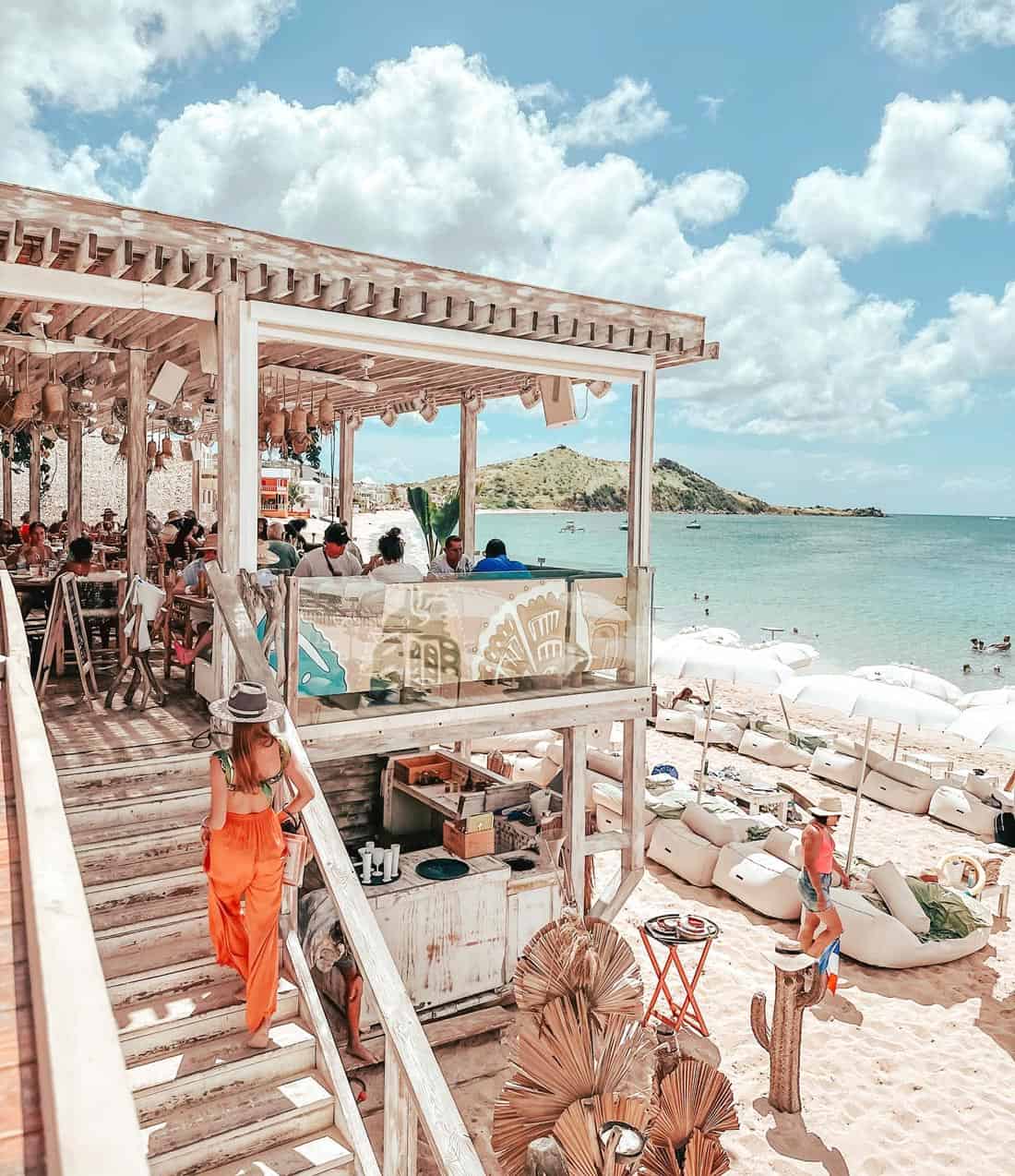 Woman in orange pants walks up stairs from the beach to Rainbow Cafe on Grand Case Beach