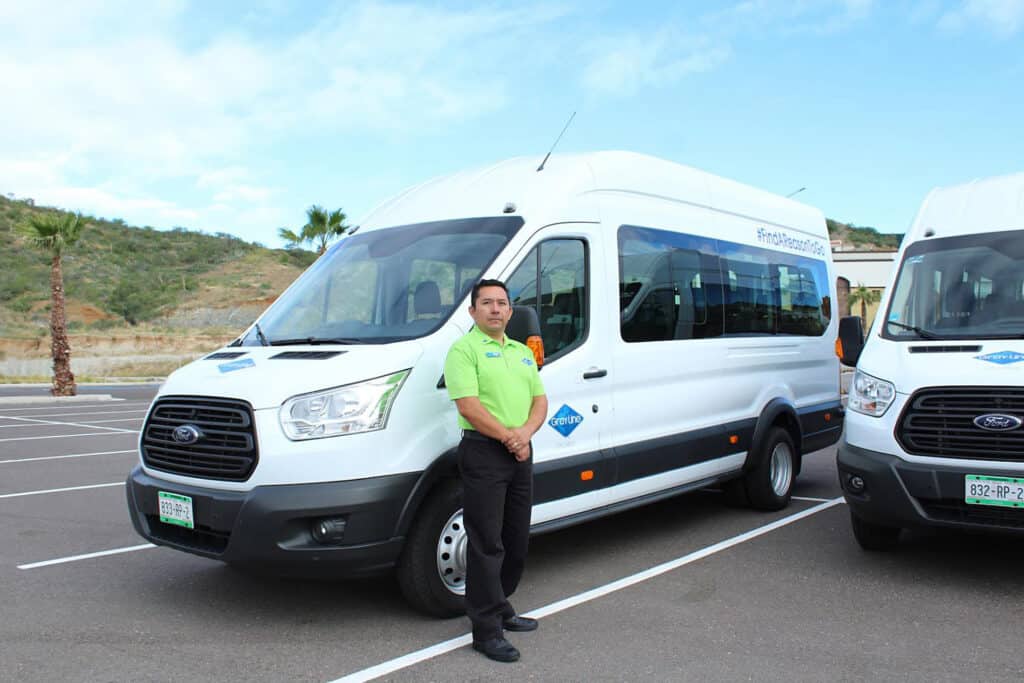 Large white van with Gray Line Los Cabos driver in a lime green shirt standing beside it