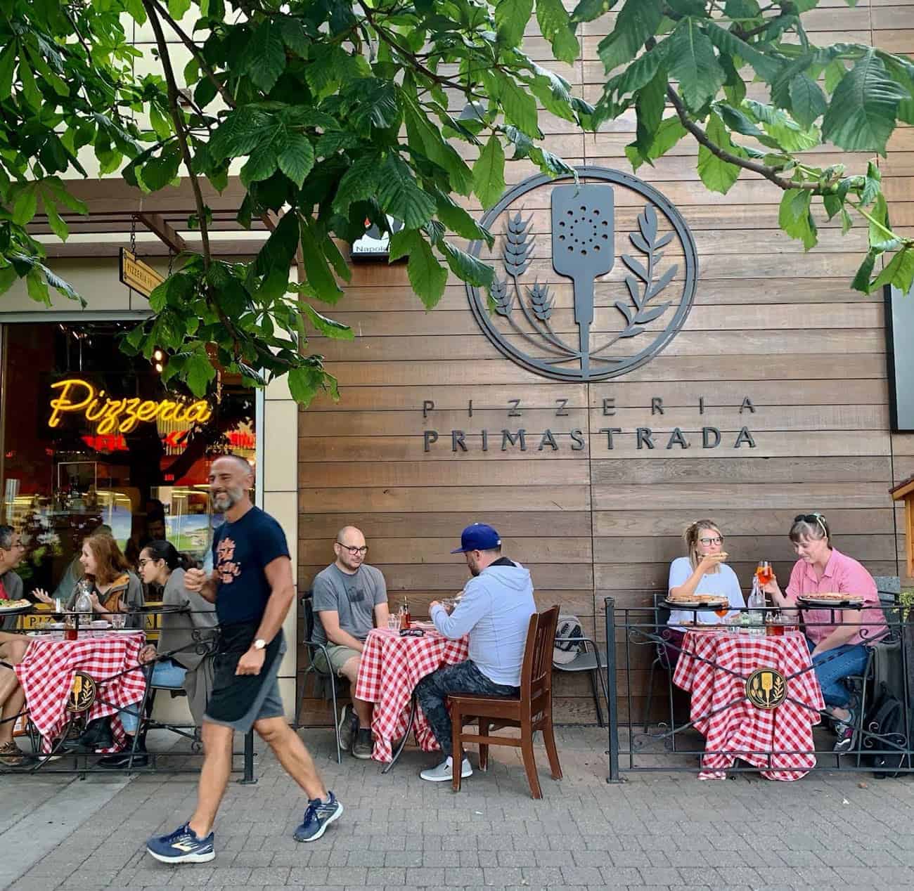 People eating pizza and drinking Aperol Spritz outside on the sidewalk at Pizzeria Prima Strada