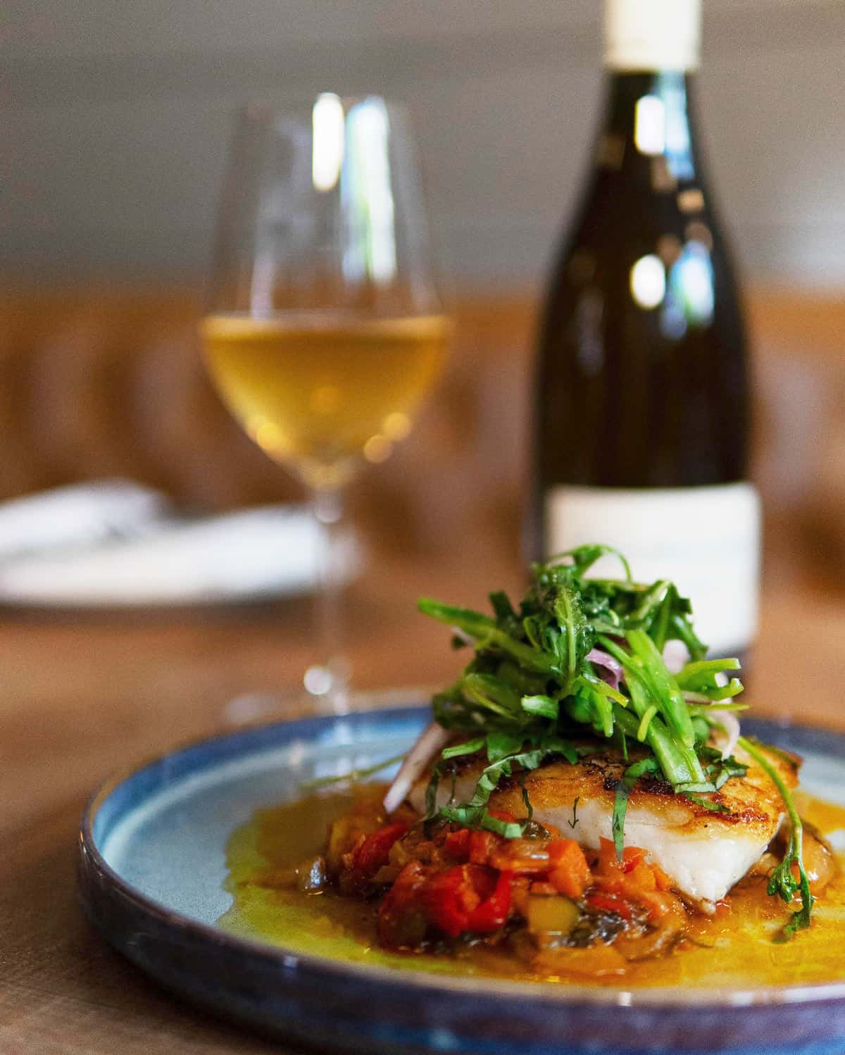 Plate of seared ling cod accompanied by a bottle of white wine