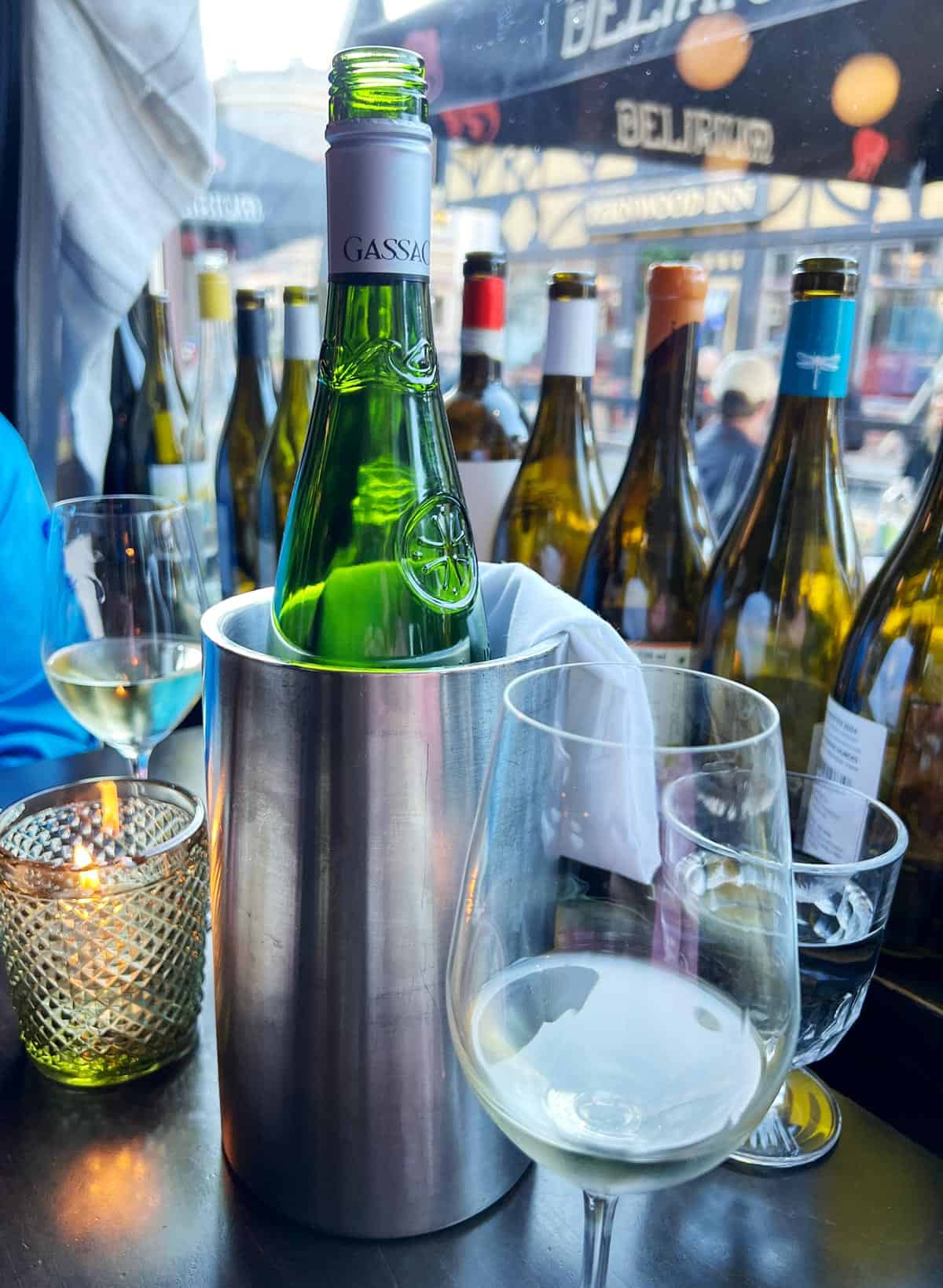 Ice bucket with bottle of wine against a backdrop display of empty wine bottles lining a window