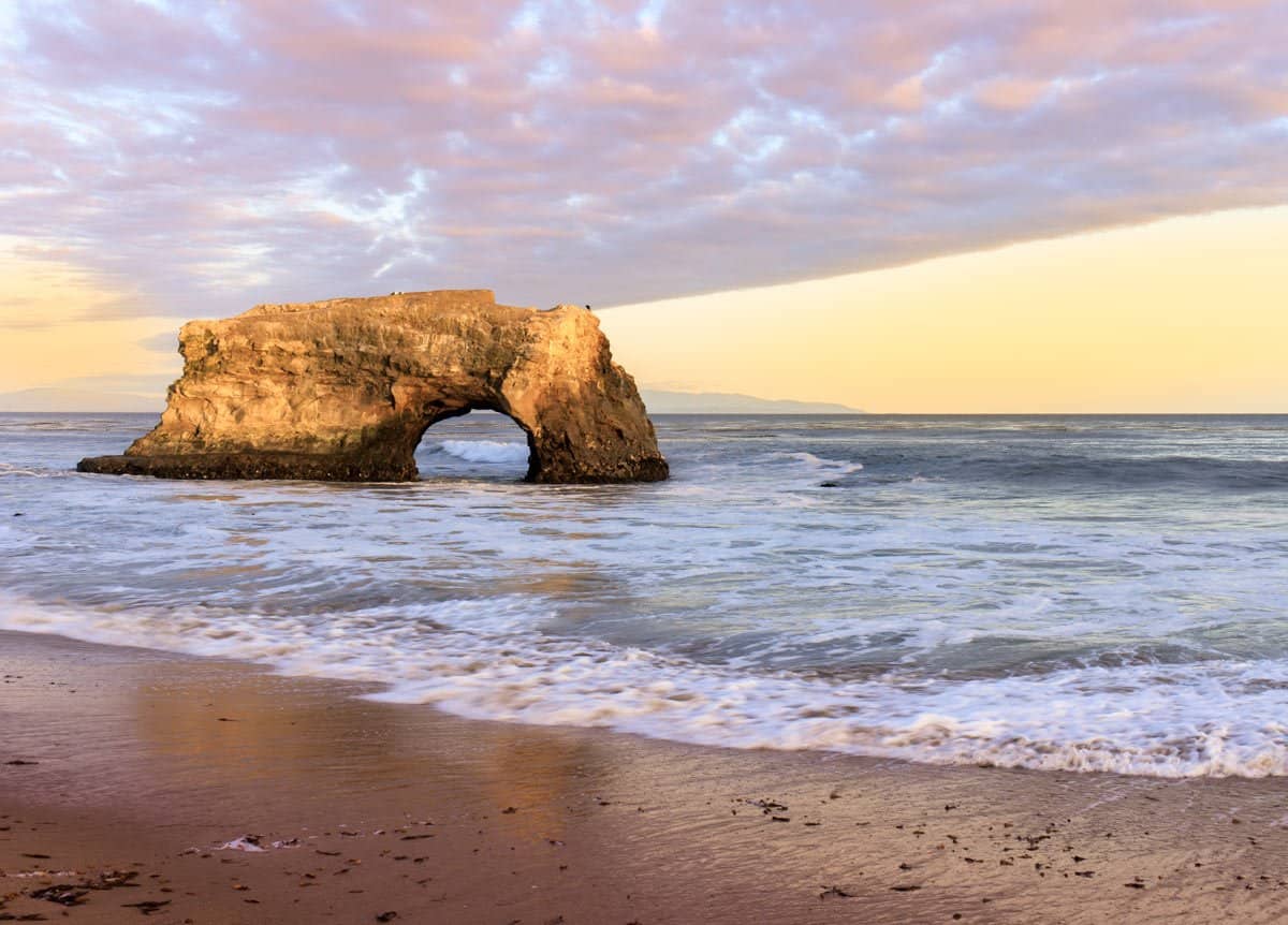 The setting sun paints the sky pink and mauve over the rock arch at Natural Bridges State Park.