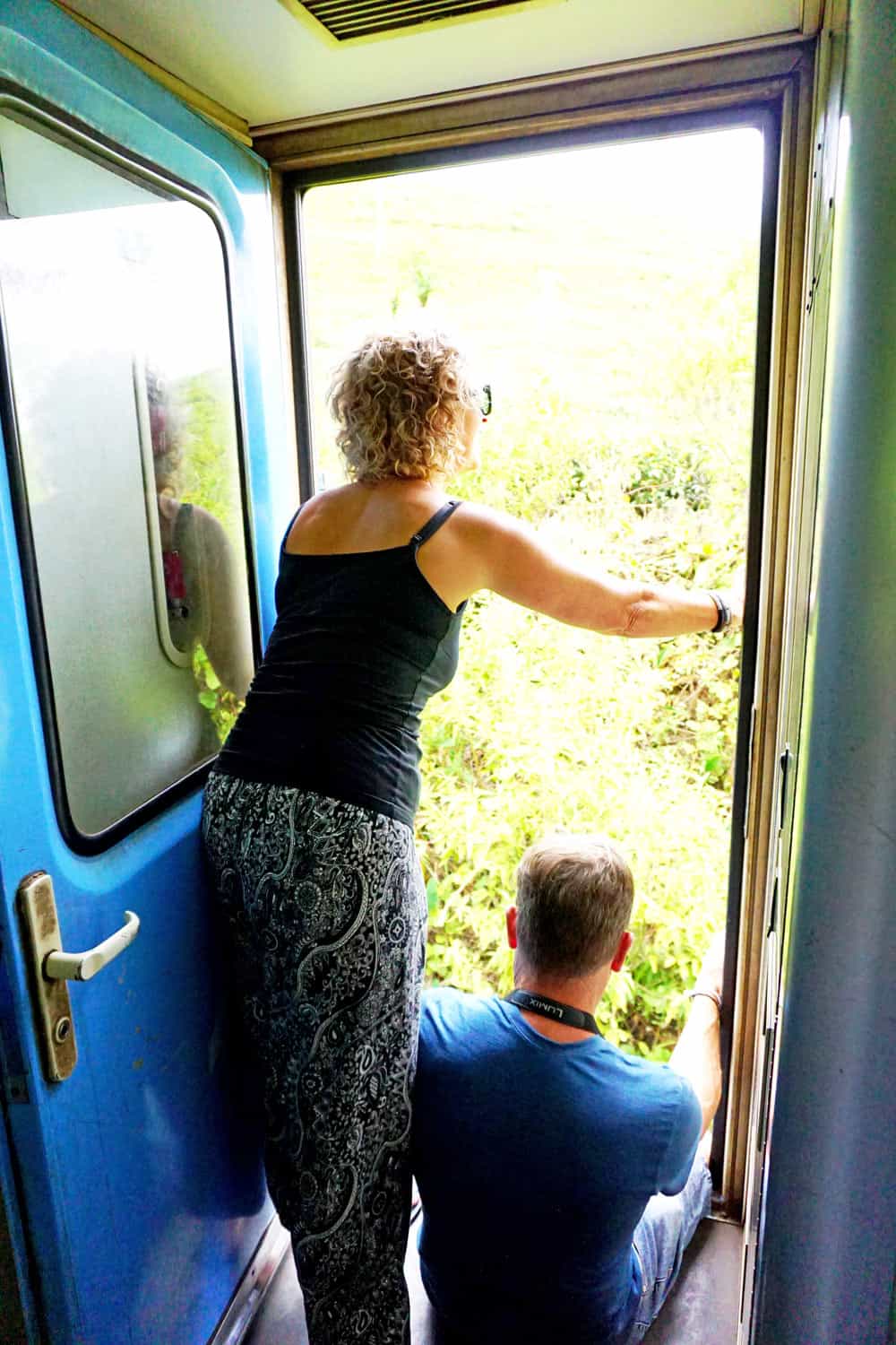Couple looking out through open door on the blue Kandy-to-Ella train