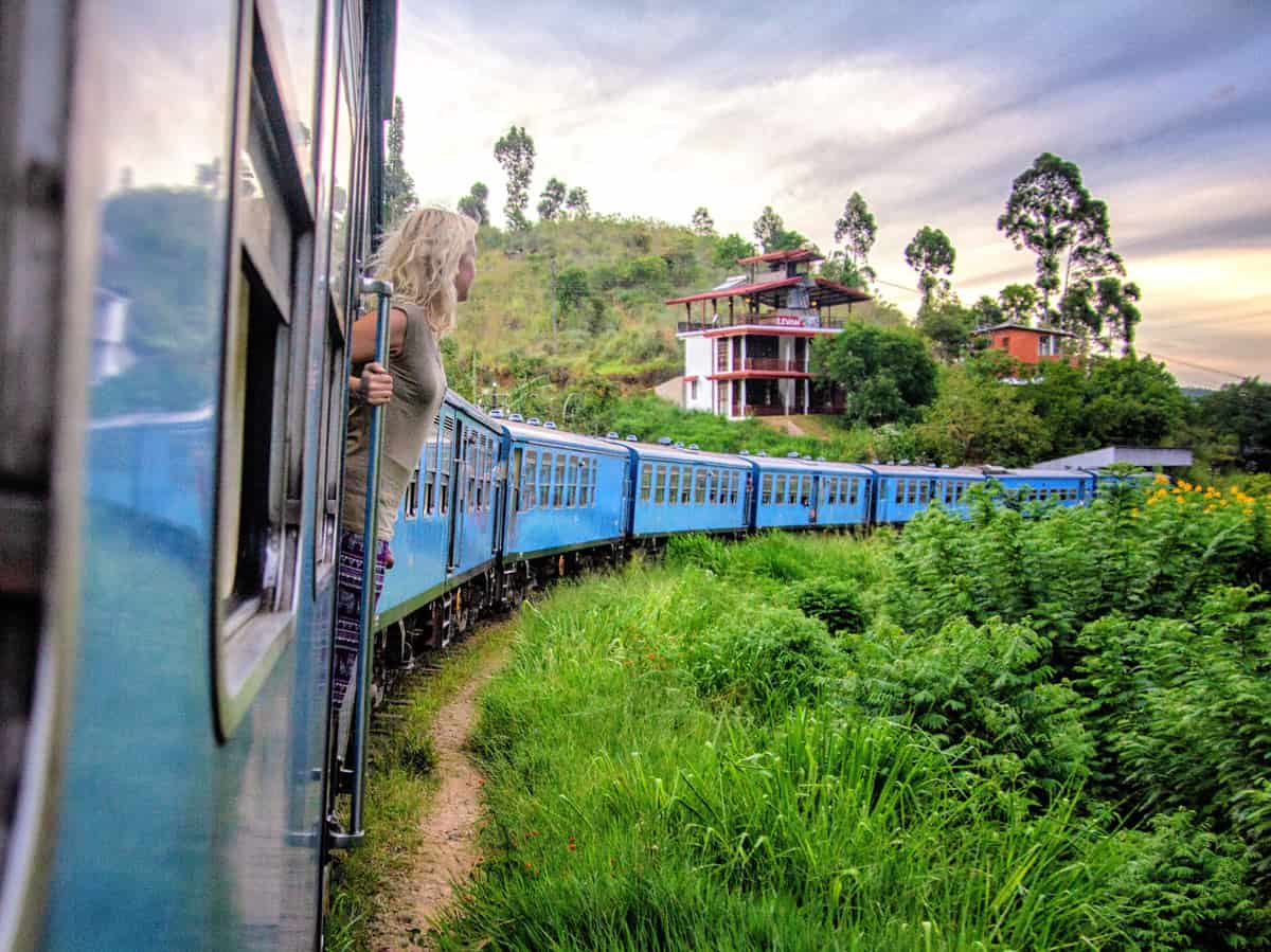 Young woman hanging out of blue Sri Lanka train