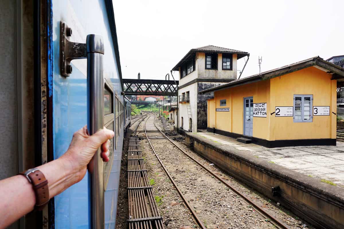 Blue train arriving in front of brown Hatton train station building