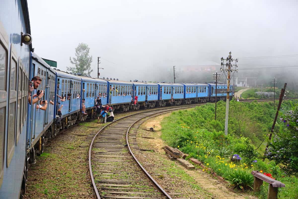 People hanging out windows and milling about the blue Kandy-to-Ella train