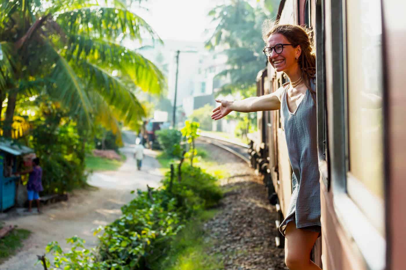 Woman in glasses hangs out a train door in Sri Lanka