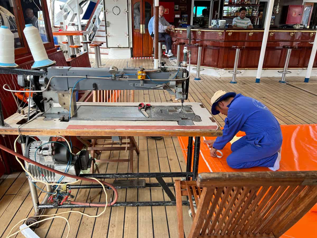 A crew member makes a new tender cover on deck, with the help of the ship's sewing machine