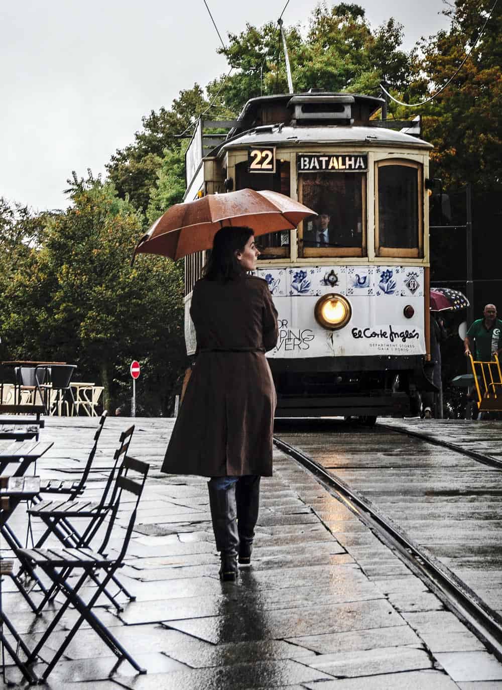 Woman with umbrella by a tram in Porto
