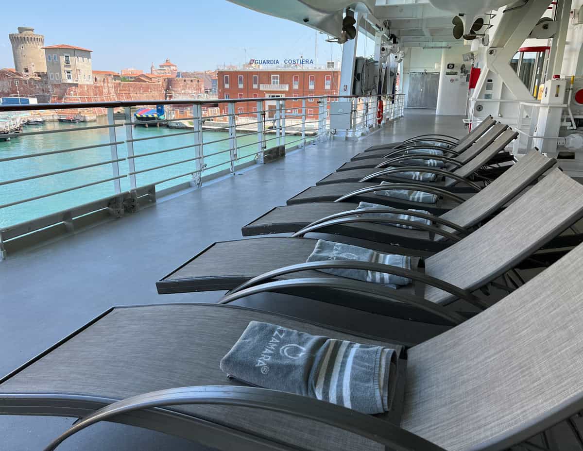 Lounge chairs with towels, underneath the lifeboats on a cruise ship deck