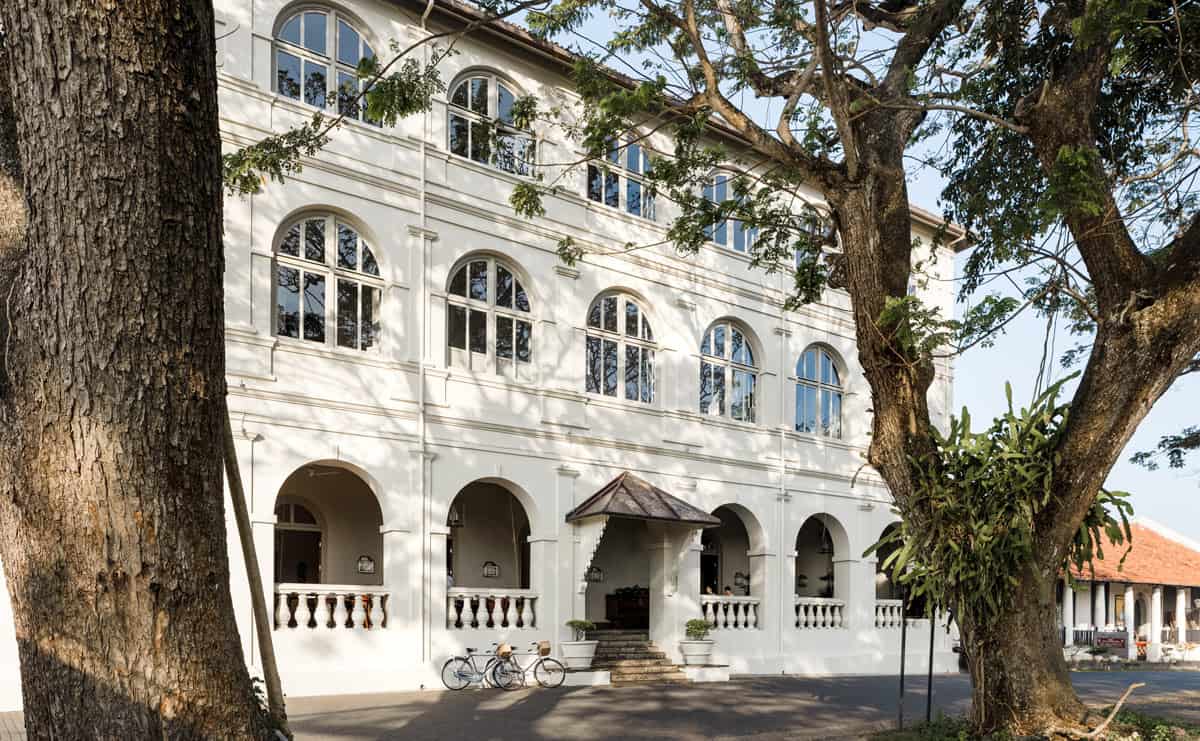 White colonial facade of Amangalla hotel in Galle Fort, framed by large tropical trees