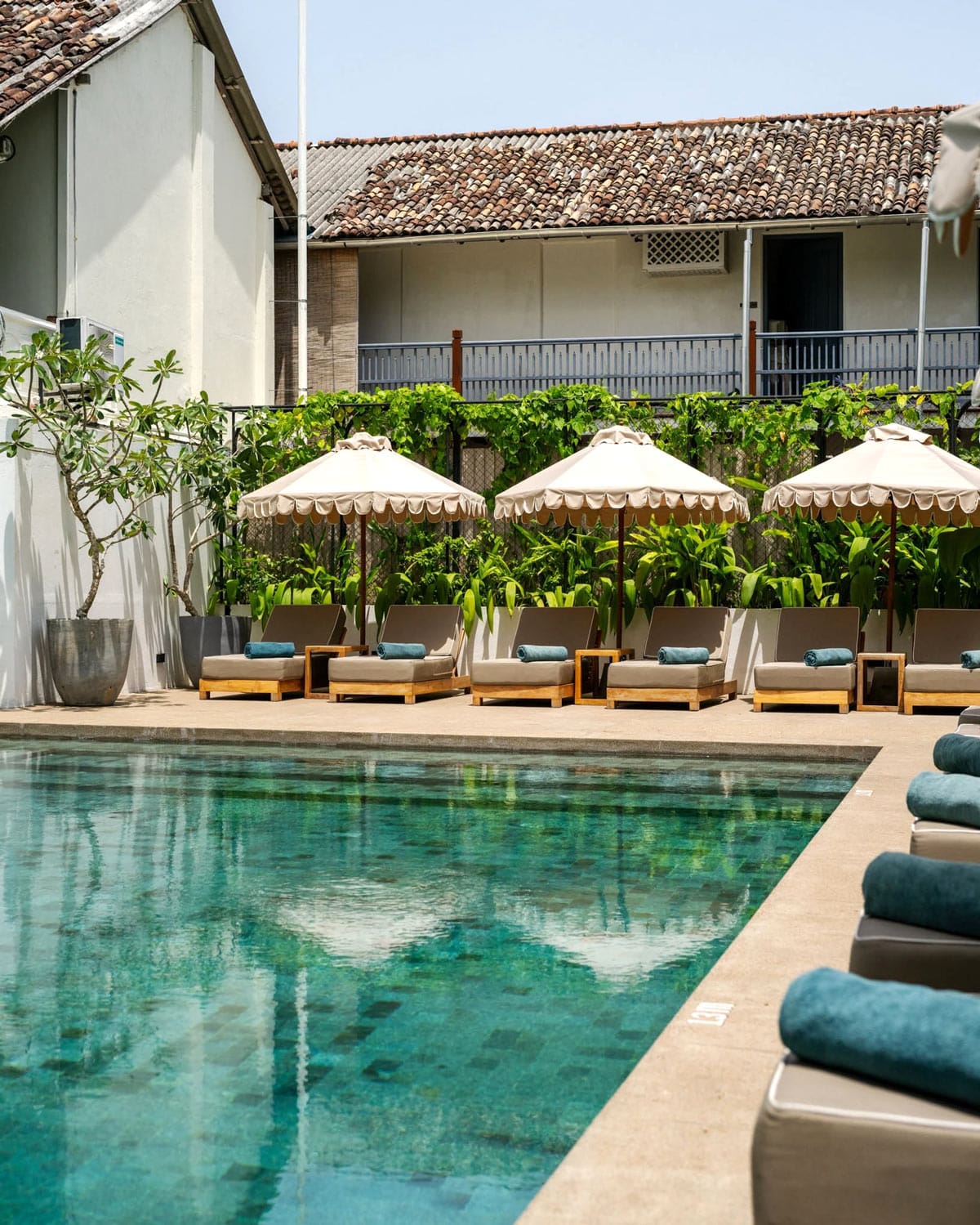 Turquoise swimming pool at Fort Bazaar, with shaded loungers and old tiled rooftops in the background