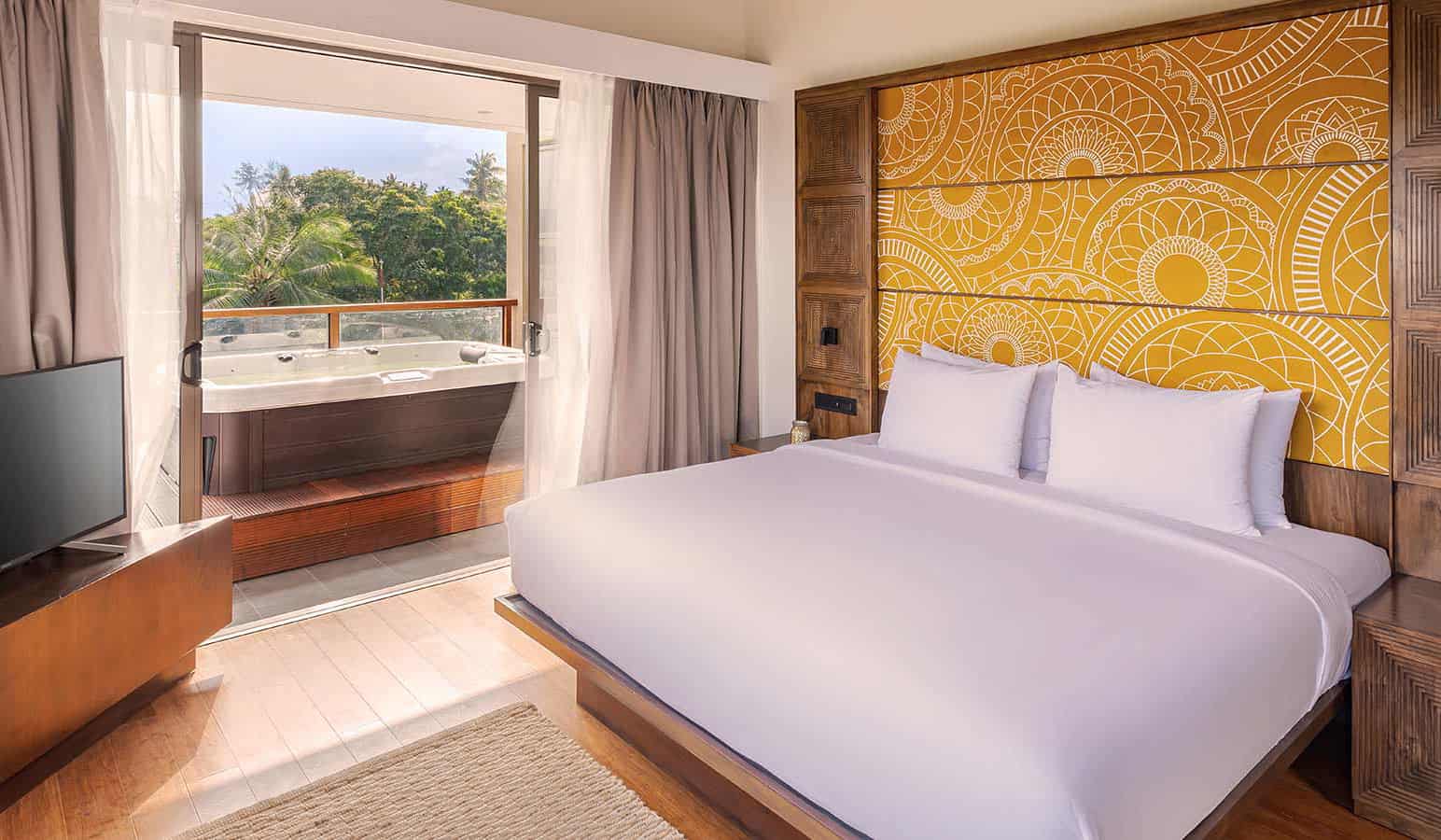 Hotel room with king bed, gold colored Sri Lankan-inspired headboard and private outdoor Jacuzzi on the deck, overlooking tropical greenery
