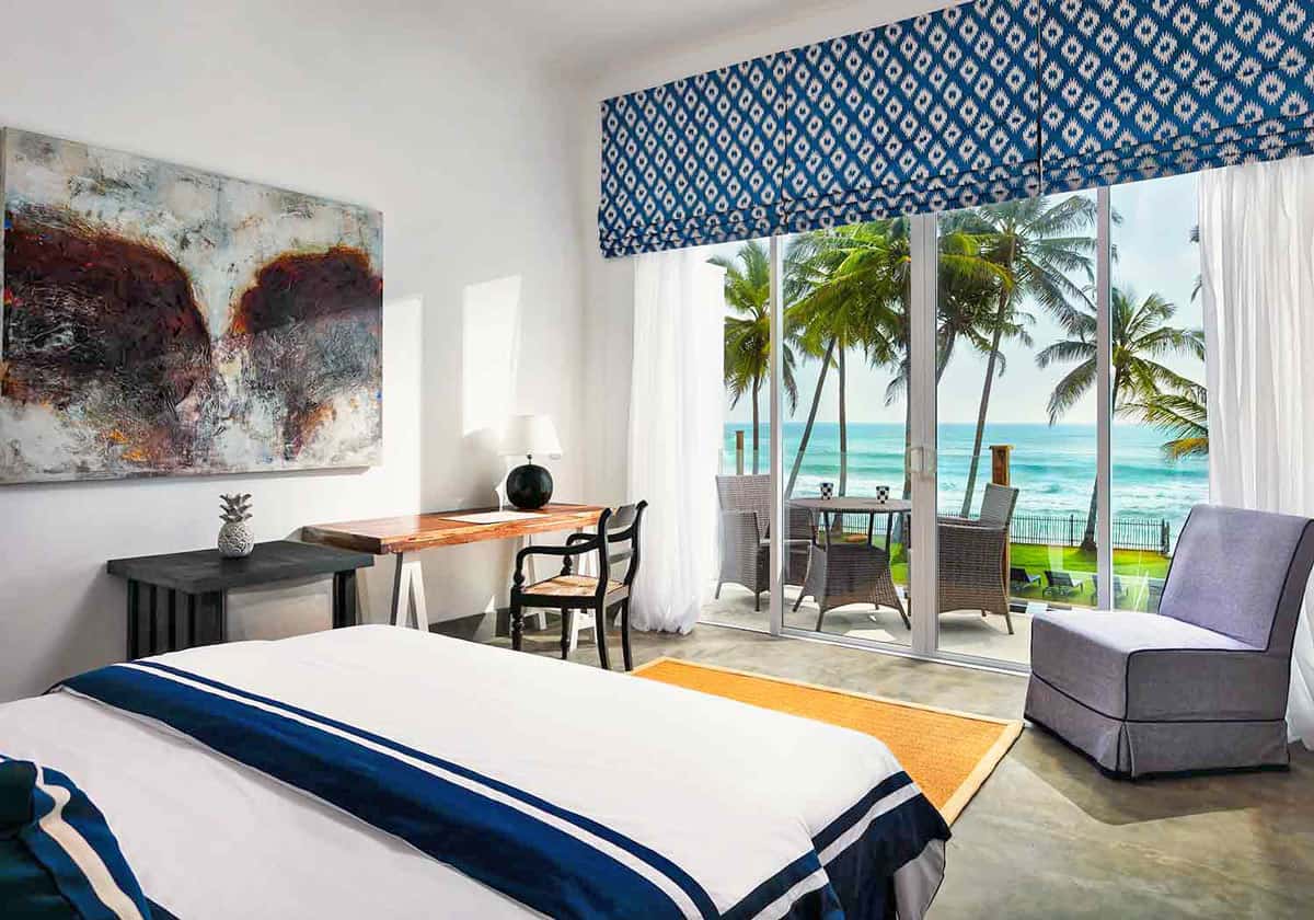 Ocean Deluxe Double room at KK Beach Galle with blue-and-white décor, private balcony, and view of palm trees and the Indian Ocean
