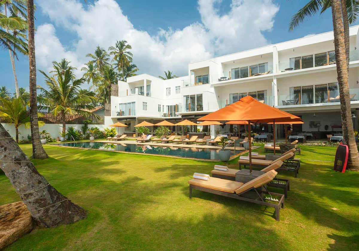 Swimming pool with orange umbrellas and sun loungers on a palm-fringed lawn