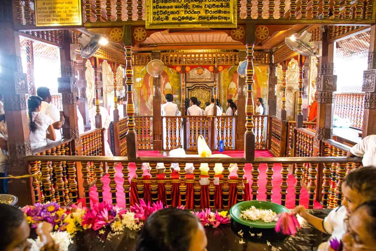 Worshippers dressed in white gather around carved wood railings inside a Sri Lanka temple.