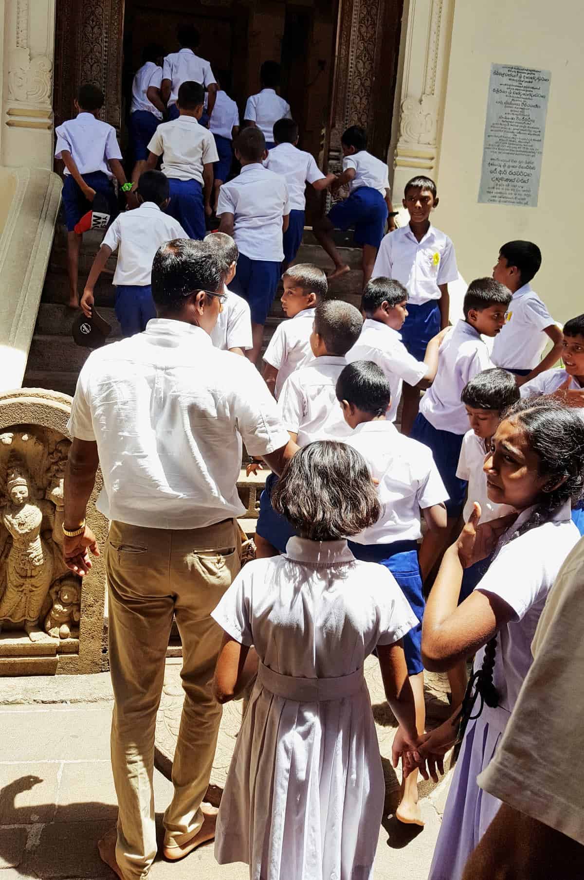 Barefoot, local schoolchildren in white uniforms line up to enter the Temple of the Tooth in Kandy.