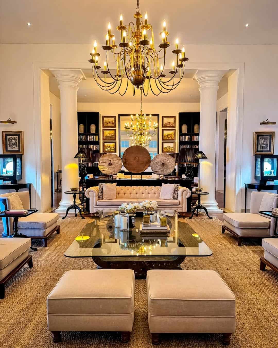 Elegant lounge with chandeliers, white columns, cream sofas, bookshelves and antique-style décor