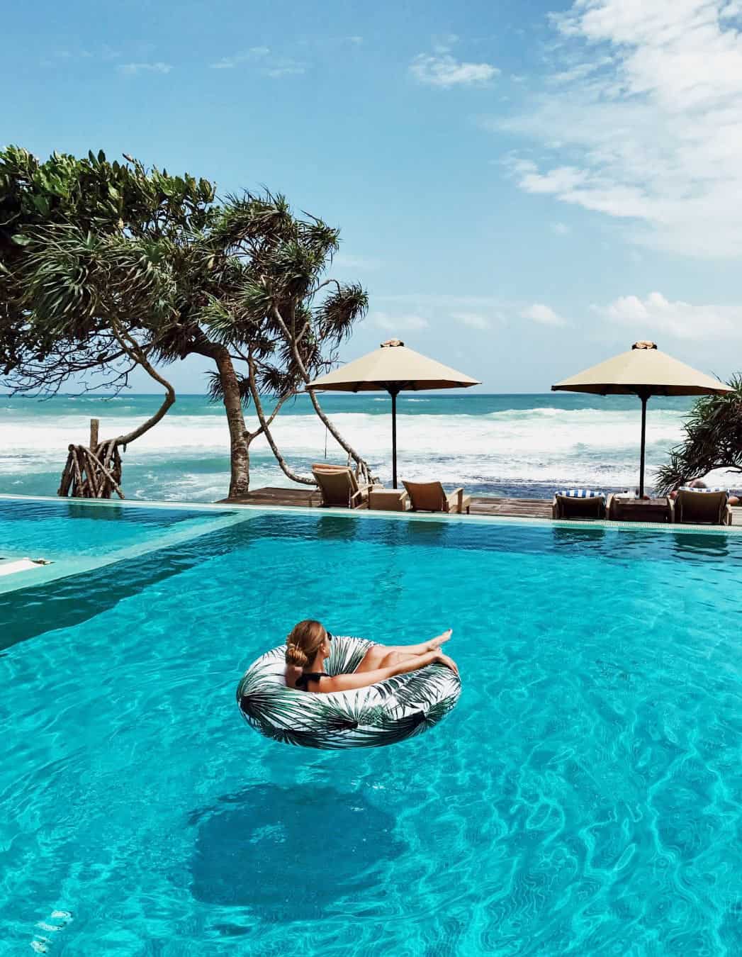Young woman floats in an inner tube in a turquoise pool, looking at the blue Indian Ocean