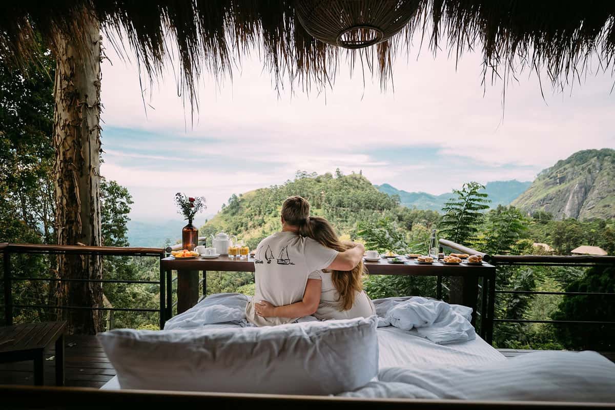 A couple enjoys breakfast in bed with mountain views in a Royal Deluxe Room, where the bed rolls right out onto the terrace at 98 Acres Resort.