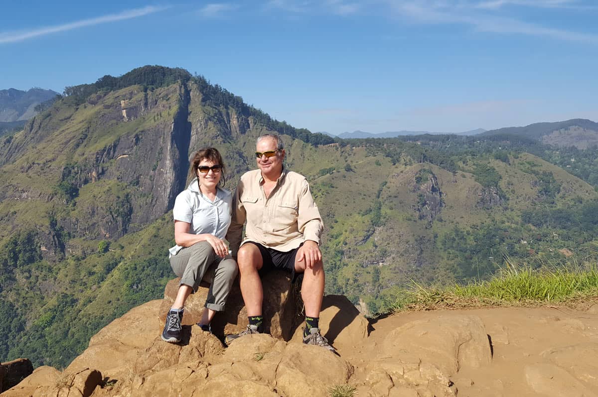 Two hikers sit at the top of Little Adam’s Peak in Ella, Sri Lanka, with sweeping mountain views behind them.