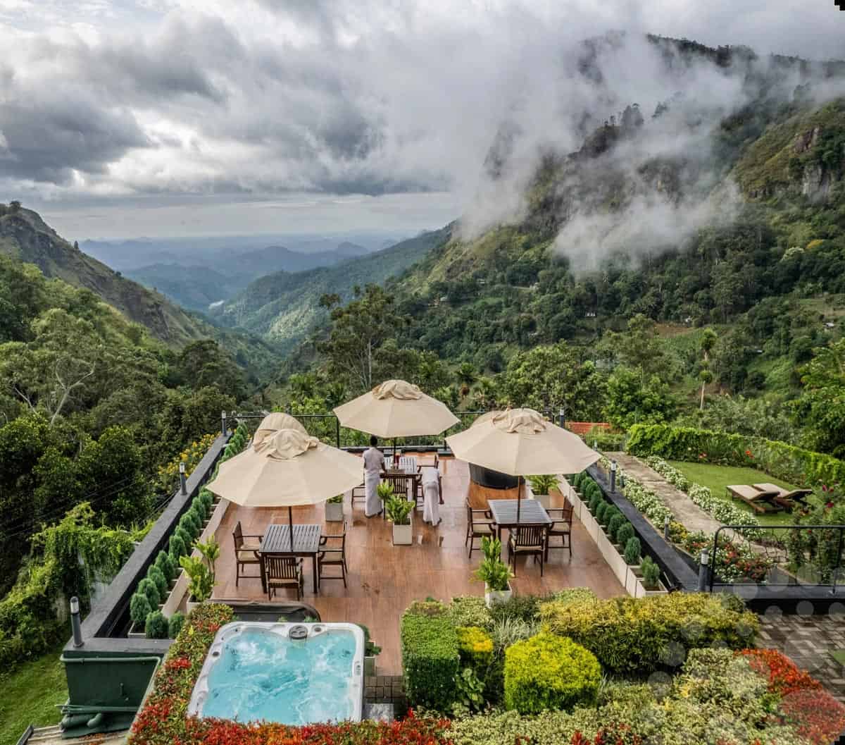 Outdoor hot tub, surrounded by red flowers, on the terrace at EKHO Ella, overlooking mist-shrouded mountains