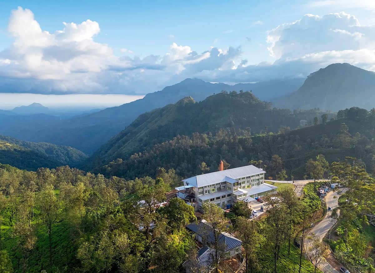 A former tea factory, with an orange chimney, surrounded by lush green hills and mountains in Ella, Sri Lanka